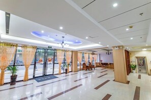 A hotel lobby with a reception desk, seating area, and a glass door entrance.