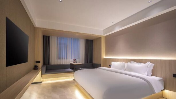 Quarto de hotel moderno com uma cama grande, televisão de tela plana, área de estar e janela com cortinas.