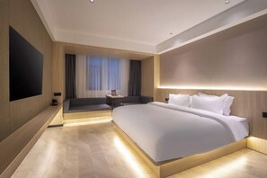 Una habitación de hotel moderna con una cama grande, un televisor de pantalla plana, una zona de estar y un ventanal con cortinas.