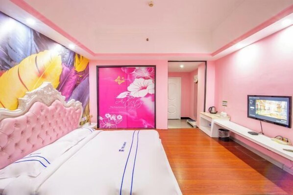 A pink-themed hotel room with a bed, a TV, and a wall with a floral mural.