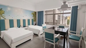 Quarto de hotel com duas camas, uma mesa de jantar, cadeiras, uma janela grande e um mural na parede.