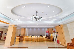 A hotel lobby with a reception desk, a chandelier, and a modern design.