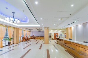 A hotel lobby with a reception desk, seating area, and a modern ceiling design.
