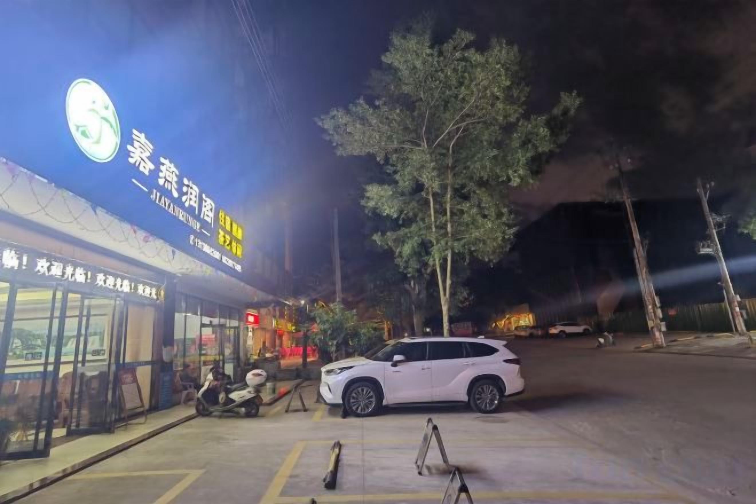 A nighttime street scene with a white car parked in front of a building with illuminated signage.