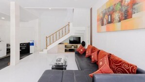 A modern living room with a black sofa, a coffee table, and a TV. There is a staircase leading to another level. - The Lavana Villa Abimanyu 3 Seminyak (Bali)