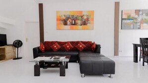 A modern living room with a sectional sofa, a glass coffee table, and a wall-mounted painting. - The Lavana Villa Abimanyu 3 Seminyak (Bali)