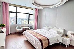 A hotel room with a bed, bedside table, chair, and a window with a city view.
