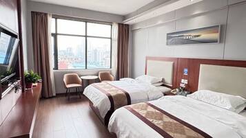 Habitación de hotel con dos camas, un escritorio, una silla, un televisor y un amplio ventanal con vista a la ciudad.