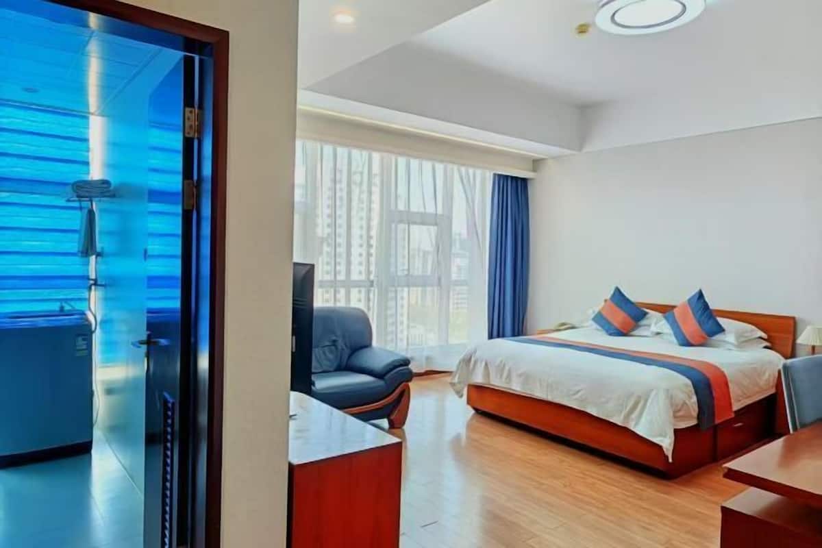 Habitación de hotel con cama, escritorio, silla, ventana con cortinas y vistas a edificios.