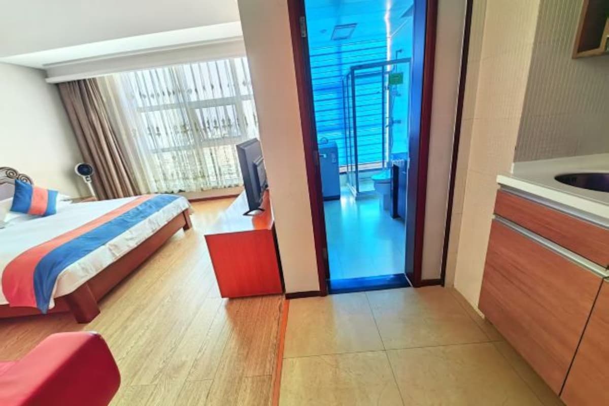 A hotel room with a bed, a desk, a chair, a bathroom with a sink, and a view of the outside.