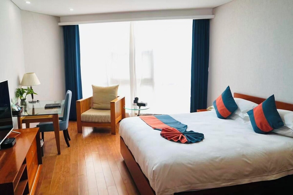 A hotel room with a bed, a desk, a chair, a TV, and a window with curtains.