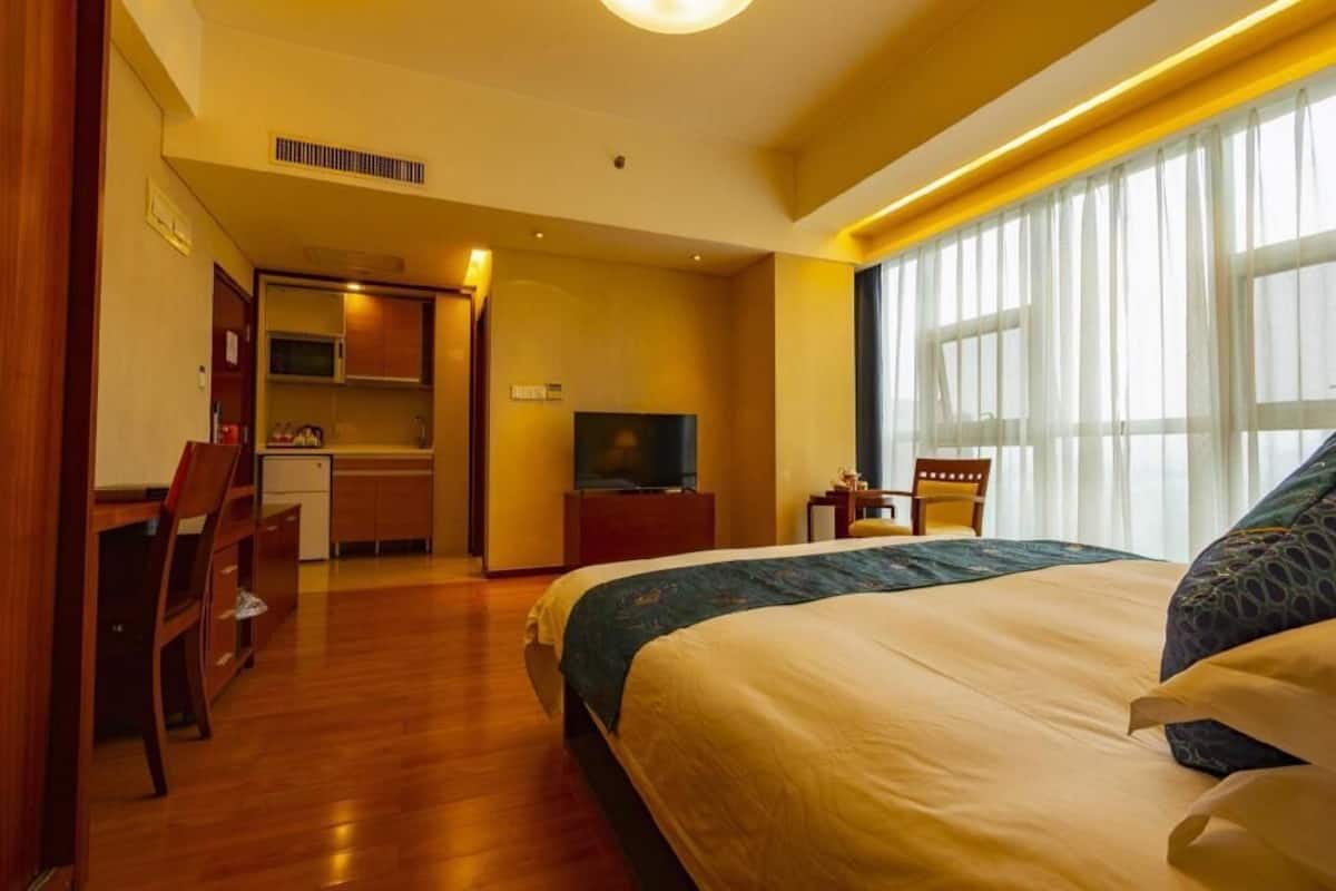 Una habitación de hotel con cama, escritorio, televisión y kitchenette.