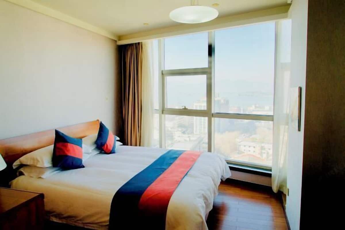 Una habitación de hotel con una cama grande, una mesita de noche, un ventanal con vista a la ciudad y una lámpara en el techo.