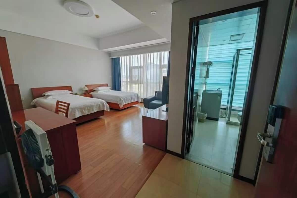 Habitación de hotel con dos camas, un escritorio con una silla, una mesita pequeña y un ventanal corredero que da a un balcón.