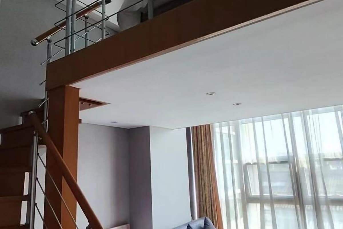 Un interior moderno con una escalera de madera, un ventanal con cortinas y vistas al exterior.