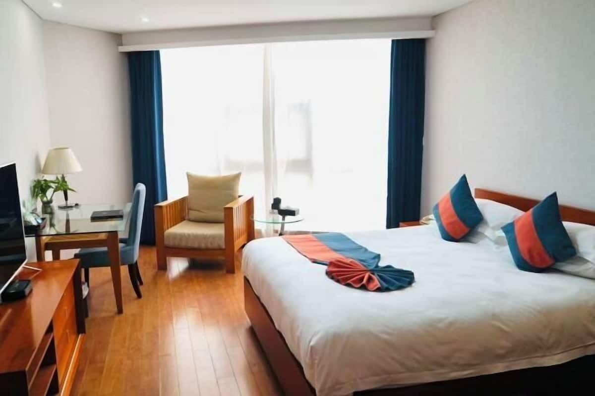 Habitación de hotel con cama, escritorio, silla, televisor y ventana con cortinas.