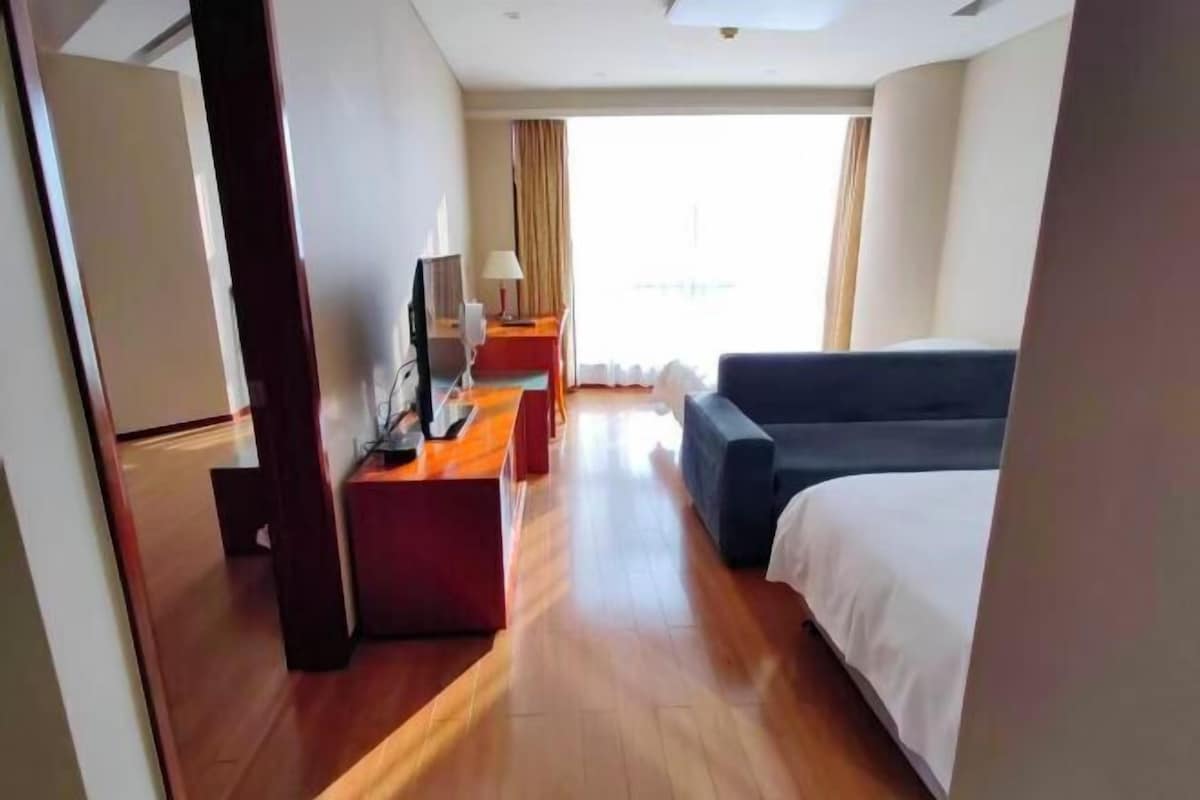 A hotel room with a bed, a desk, a TV, and a window with curtains.