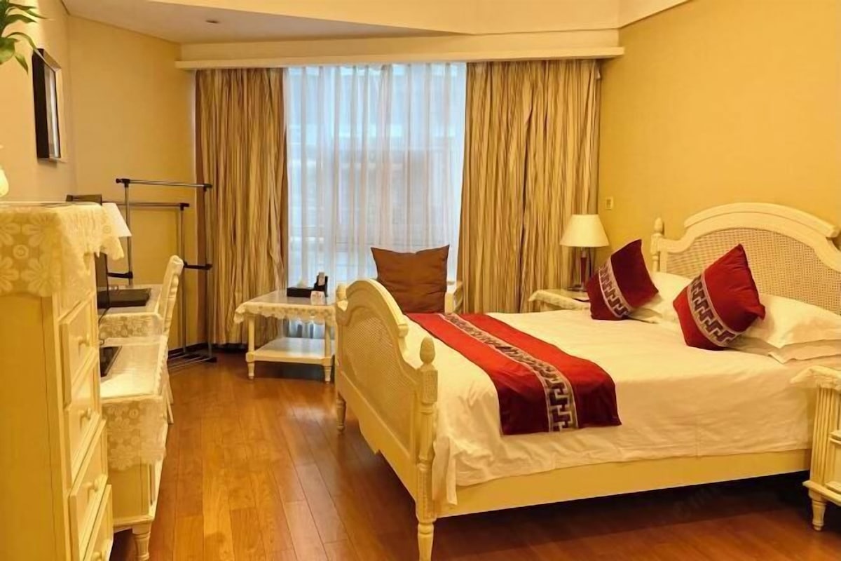 A hotel room with a bed, bedside table, lamp, and a window with curtains.
