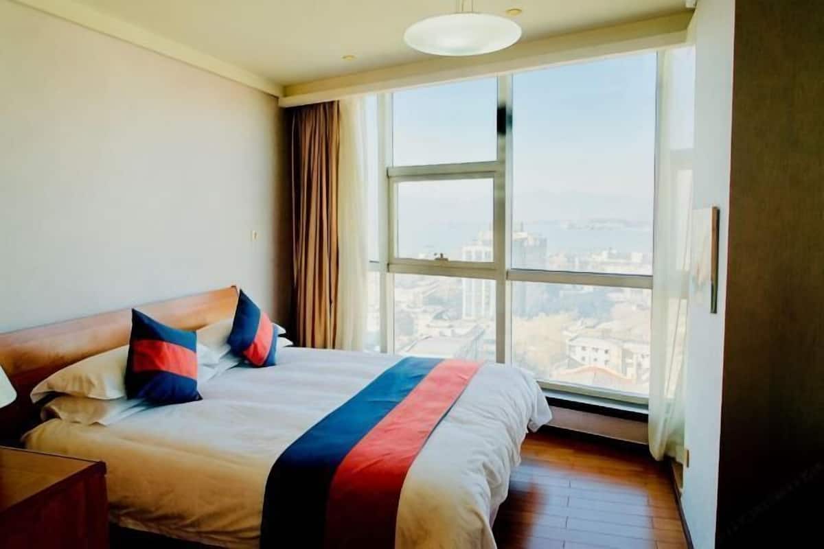 Habitación de hotel con una cama grande, una mesita de noche y vistas a un paisaje urbano a través de un ventanal amplio.