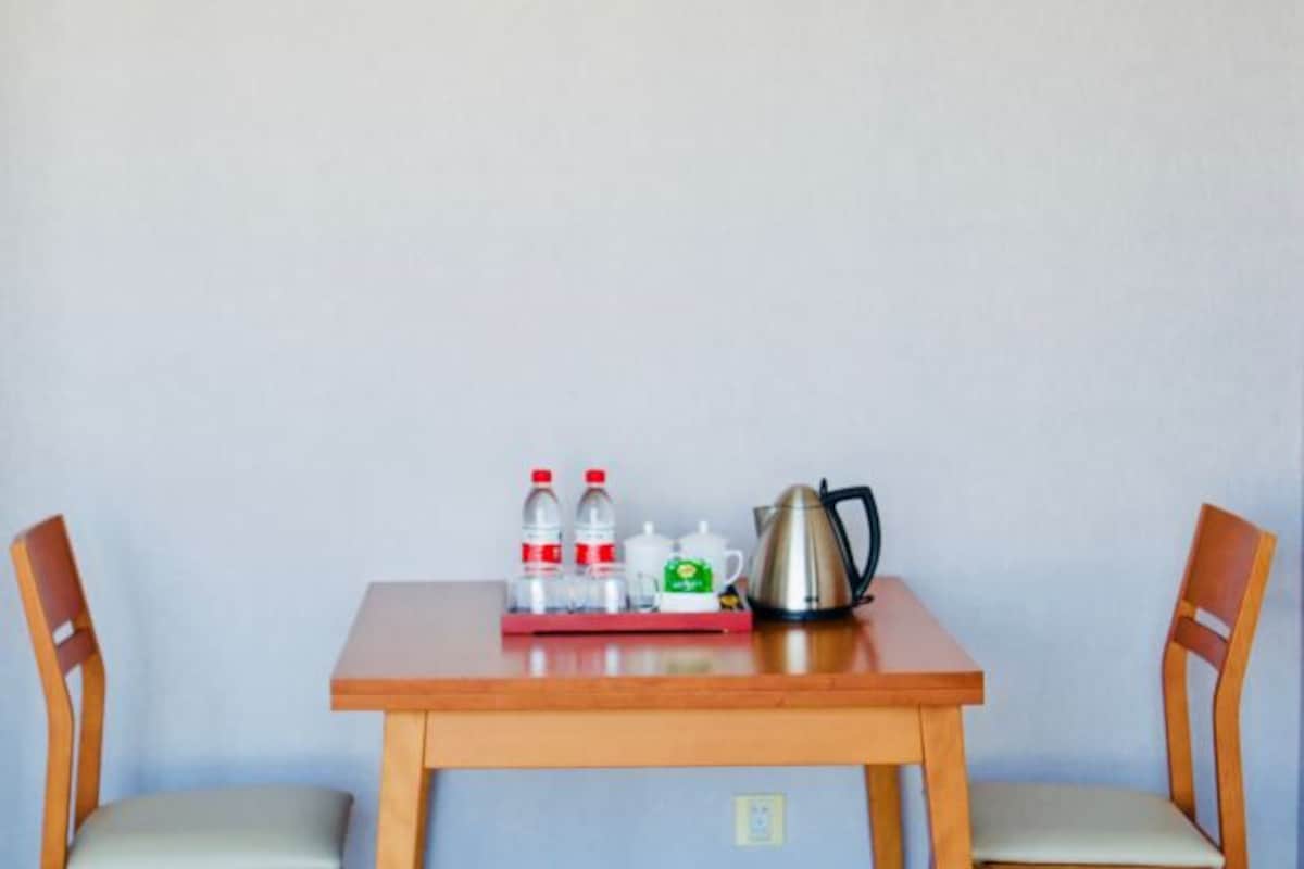 A wooden table with a tray holding bottles, a mug, and a kettle. Two wooden chairs are positioned on either side of the table.