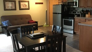 Un espace de vie compact comprenant une table et des chaises, un canapé, un coin cuisine équipé d’appareils électroménagers et des tableaux encadrés accrochés au mur.