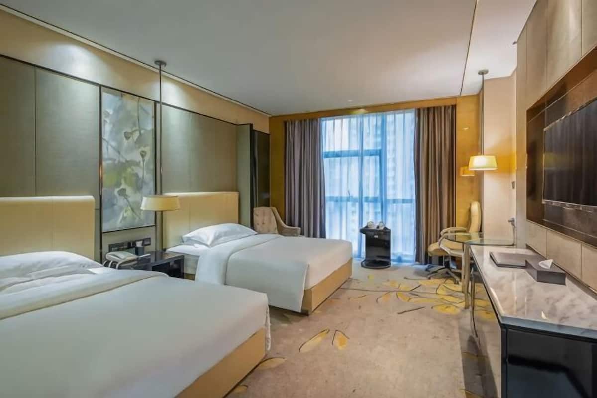 A hotel room with two beds, a desk, a chair, a large window with curtains, and a minibar.
