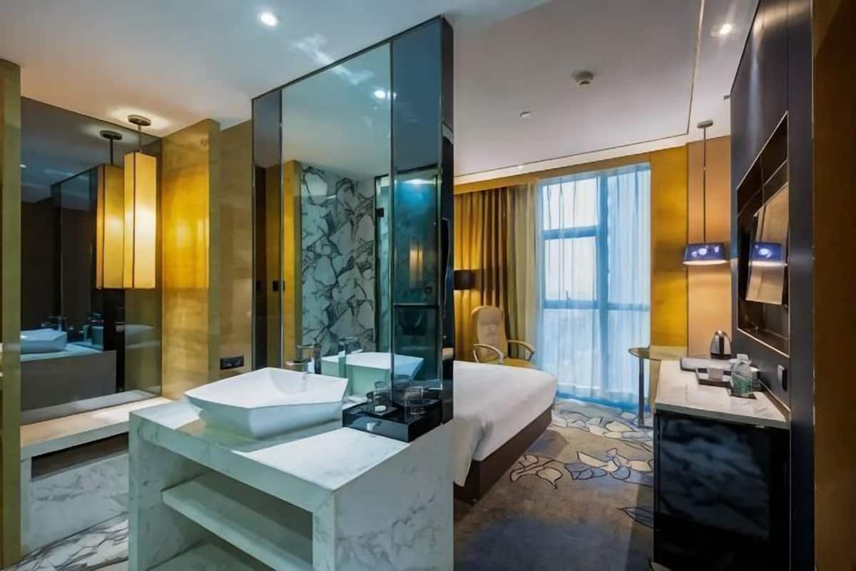A modern hotel bathroom with a large mirror, two sinks, a bathtub, and a large window.