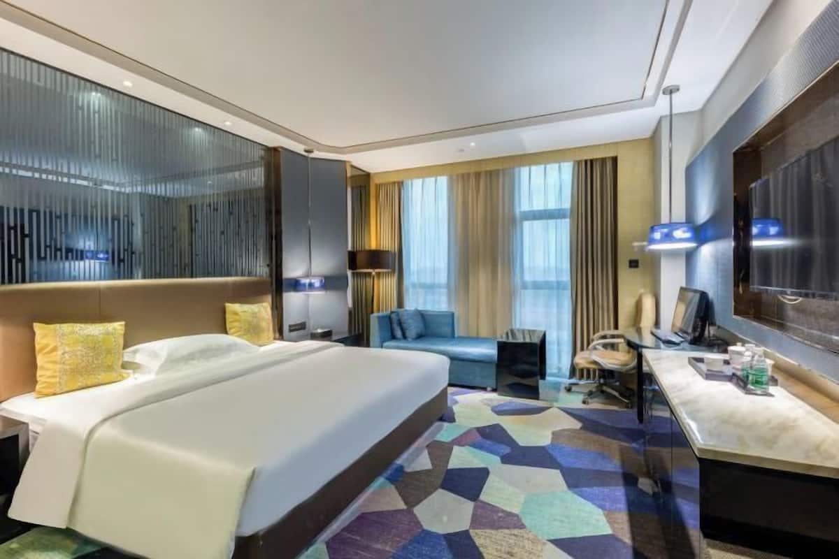 A hotel room with a large bed, a desk, a sofa, and a television.
