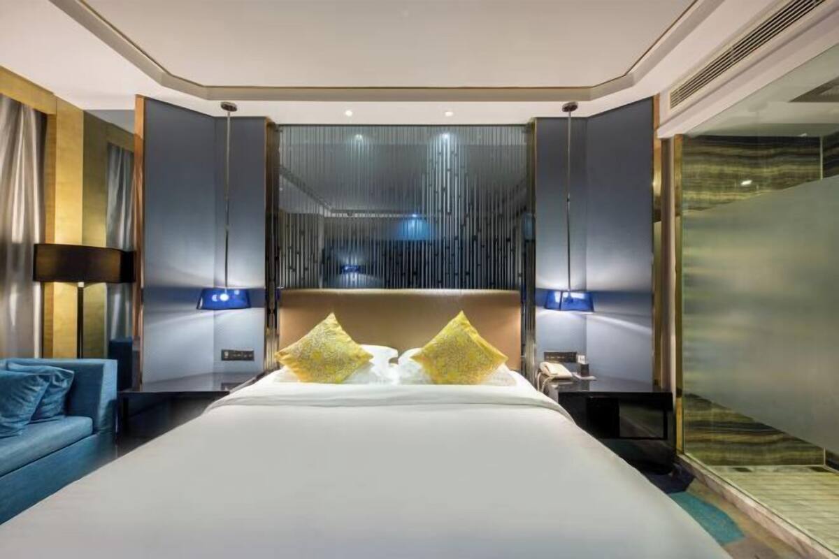 A modern hotel room with a large bed, a blue sofa, and a glass partition wall.