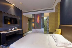 A modern hotel room with a large bed, a flat-screen TV mounted on the wall, a small desk with a mirror, and a decorative wall piece. - Tianhai Hotel (Jiujiang The Second Yangtze River Bridge Harbor) (Jiujiang)
