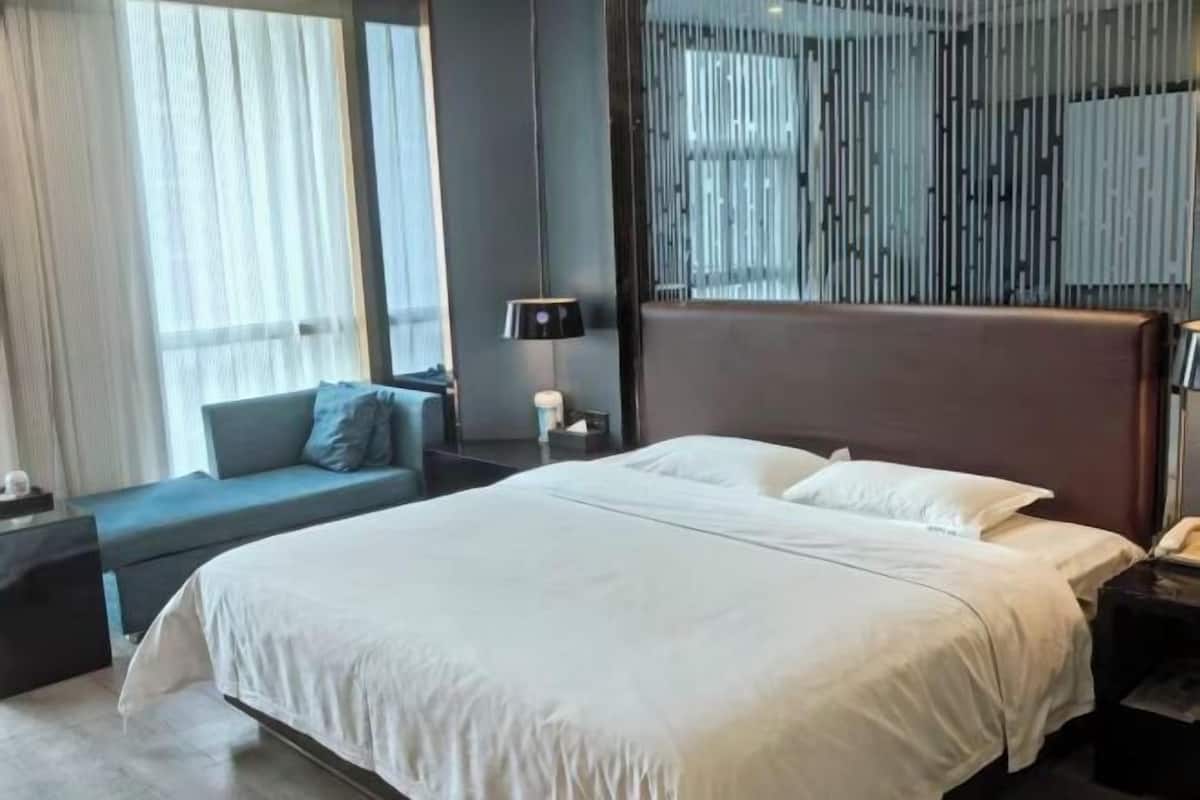 A hotel room with a large bed, a sofa, a lamp, and a window with curtains.