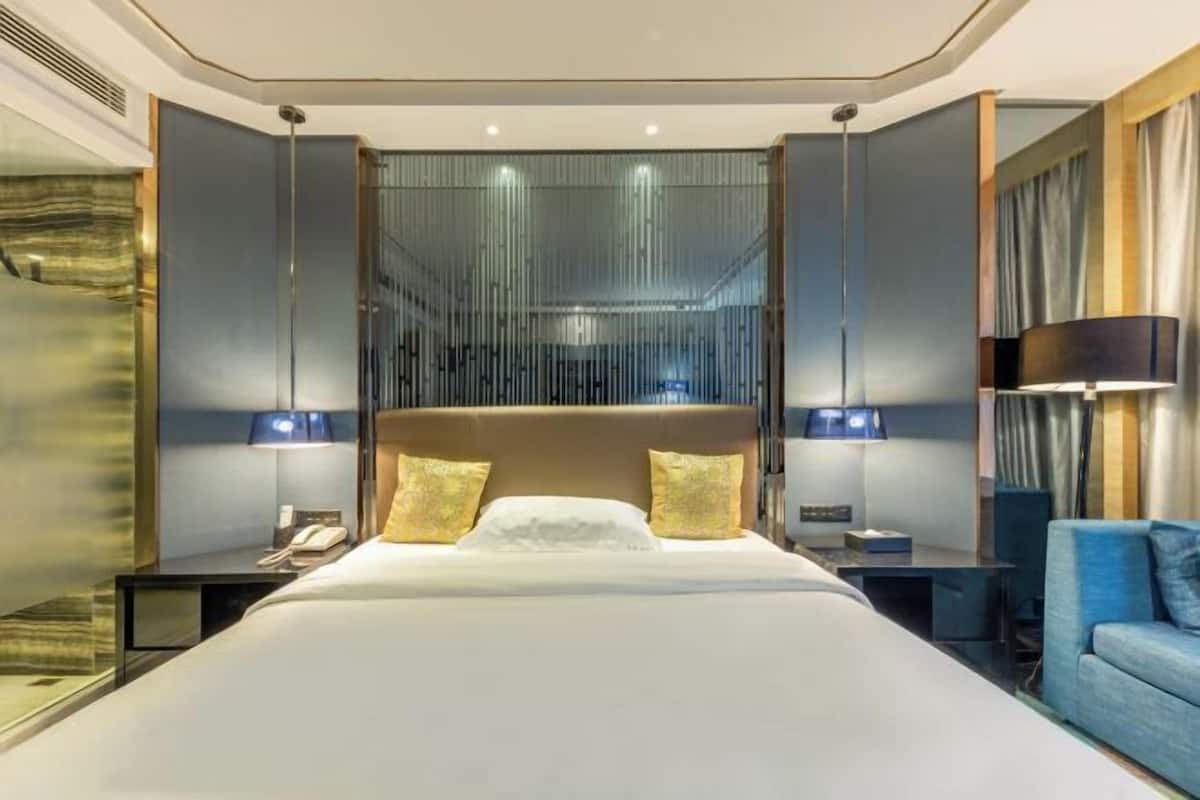A modern hotel room with a large bed, bedside tables with lamps, a blue sofa, and a decorative wall panel.