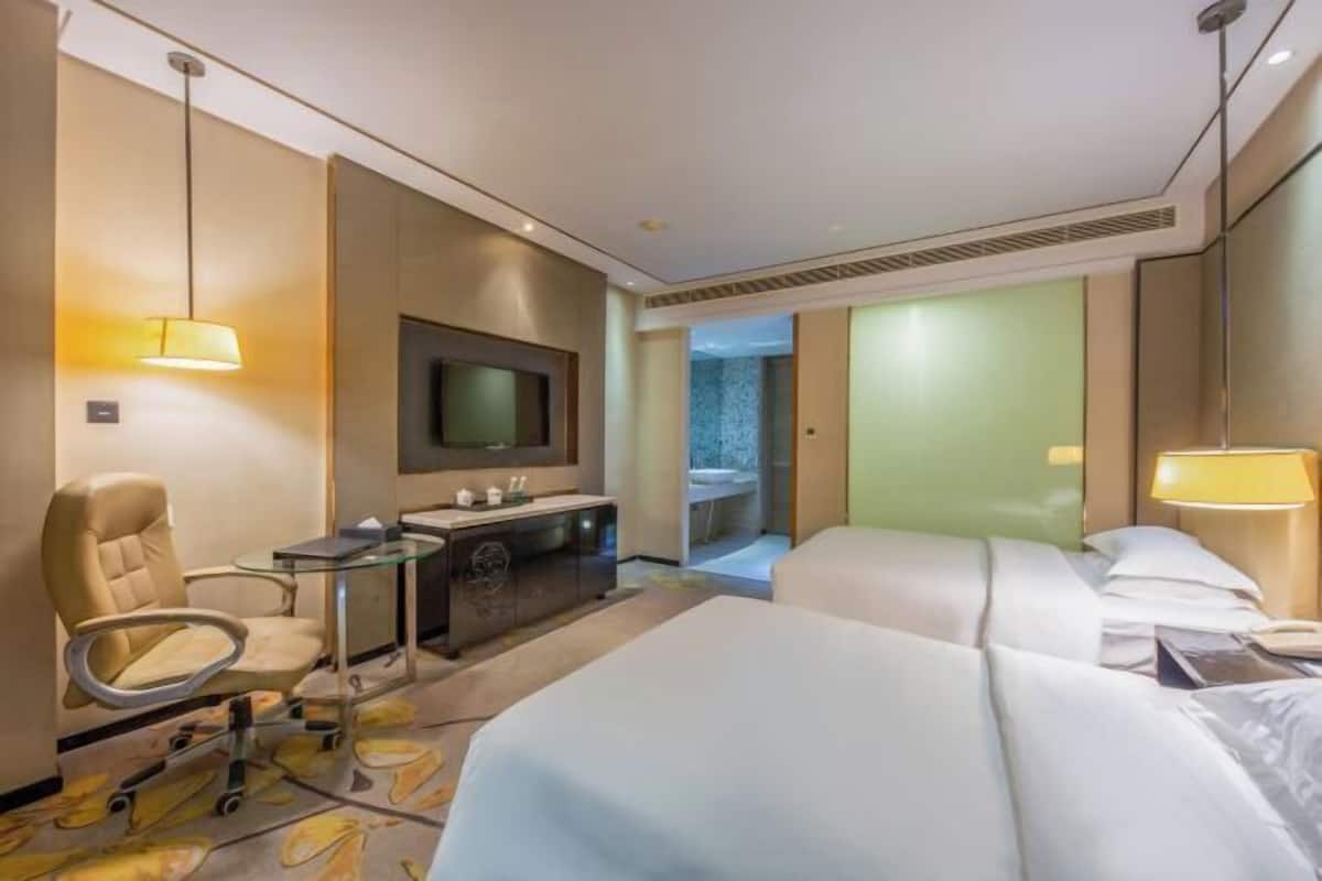 A hotel room with a bed, a desk, a chair, a TV, and a bathroom visible through an open door.