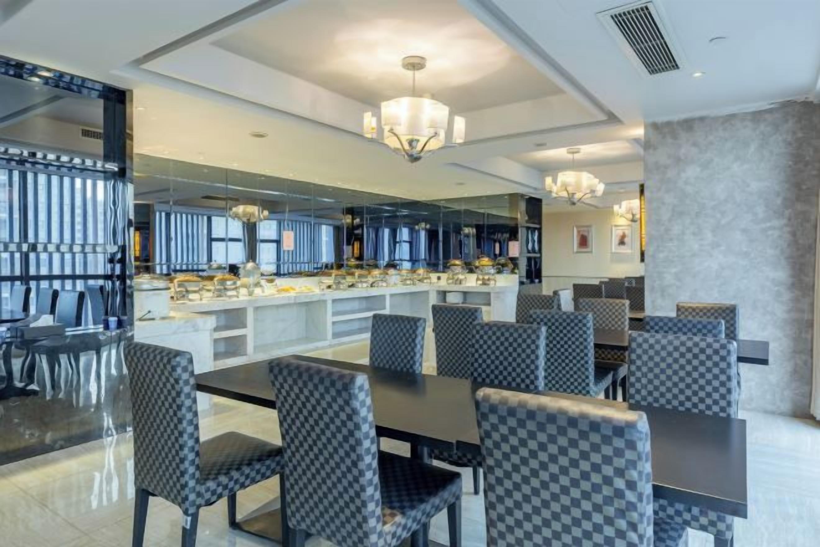 A modern dining area with a long table and checkered chairs, a bar area with a counter, and a chandelier.