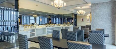 A modern dining area with a long table and checkered chairs, a bar area with a counter, and a chandelier.