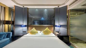 A modern hotel room with a large bed, a blue sofa, and a glass partition.