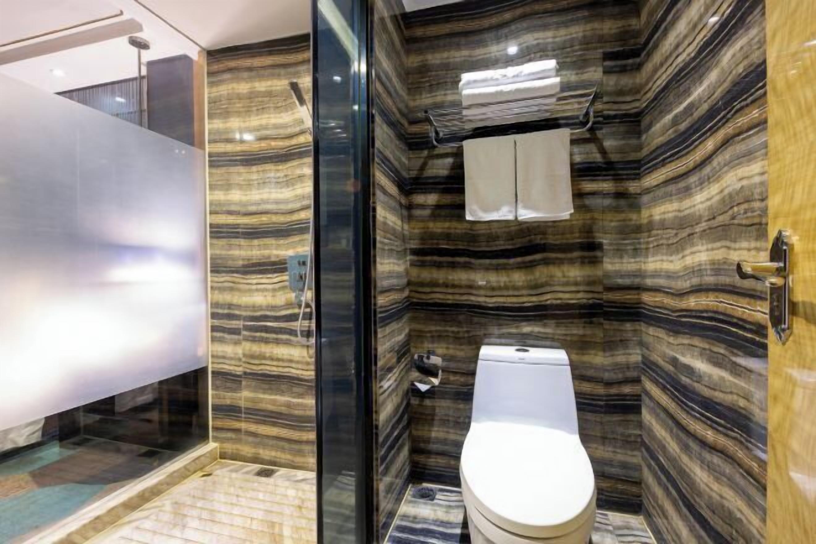 A bathroom with a marble wall, a toilet, and a glass shower enclosure.