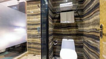 A bathroom with a marble wall, a toilet, and a glass shower enclosure.