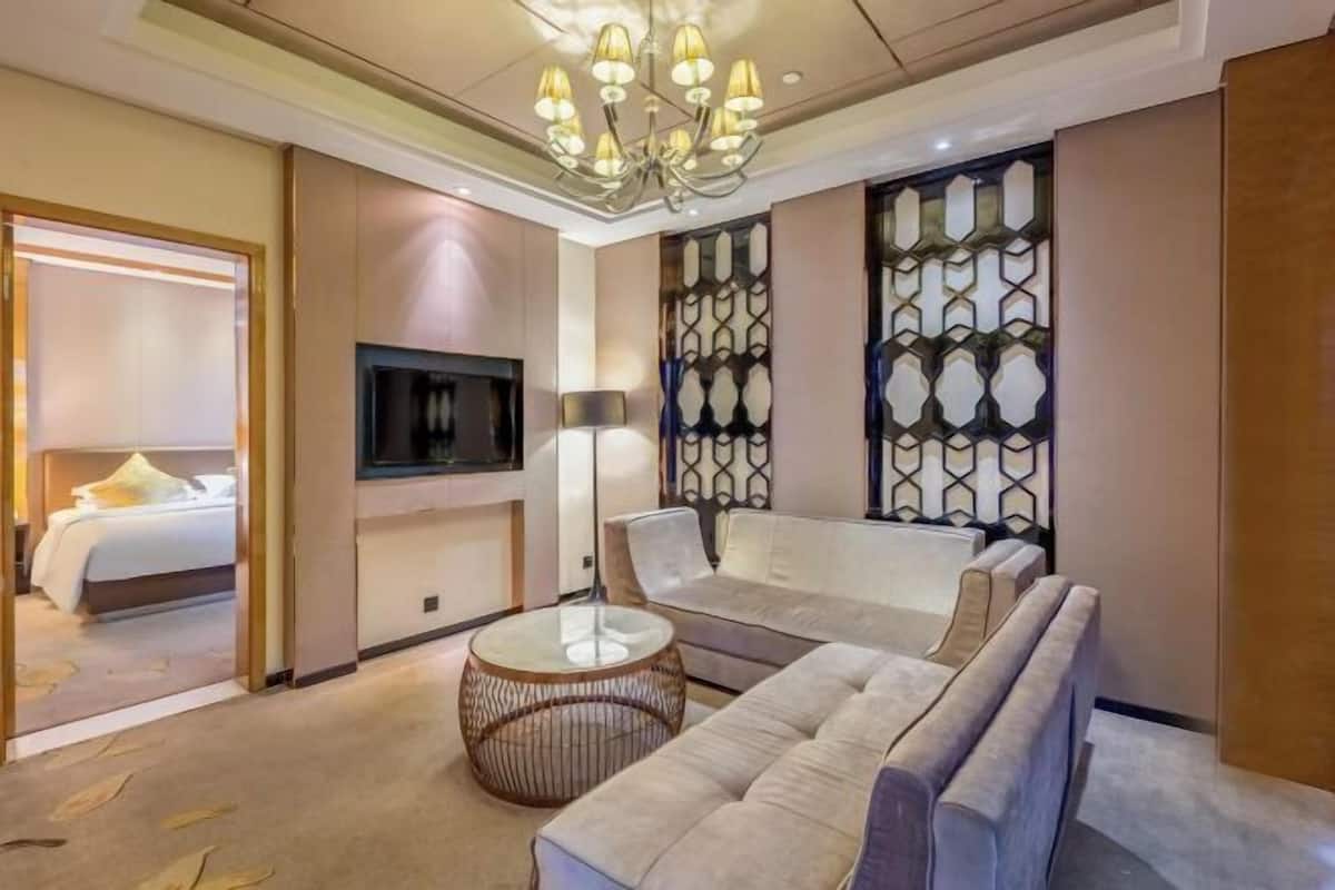 A hotel room with a sofa, a TV, a lamp, and a decorative wall.