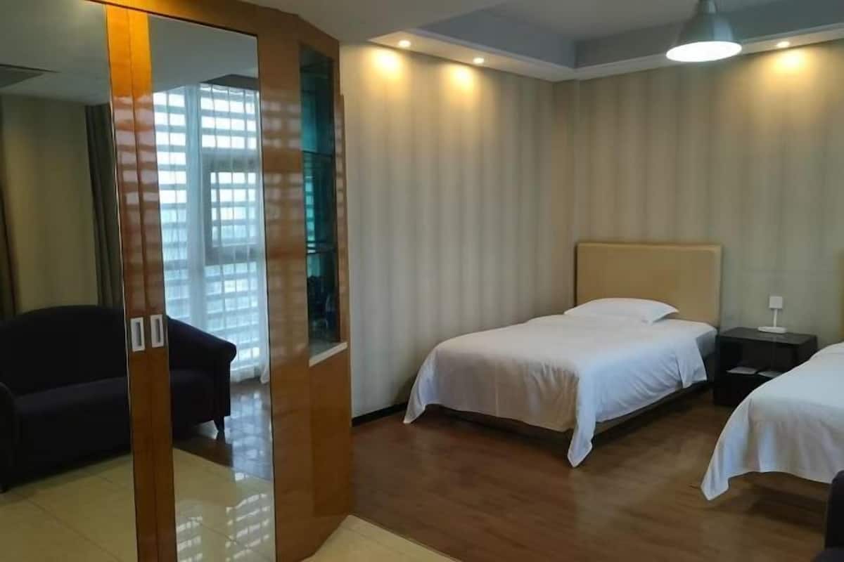 A hotel room with two beds, a wooden wardrobe, a mirror, and a window with blinds.