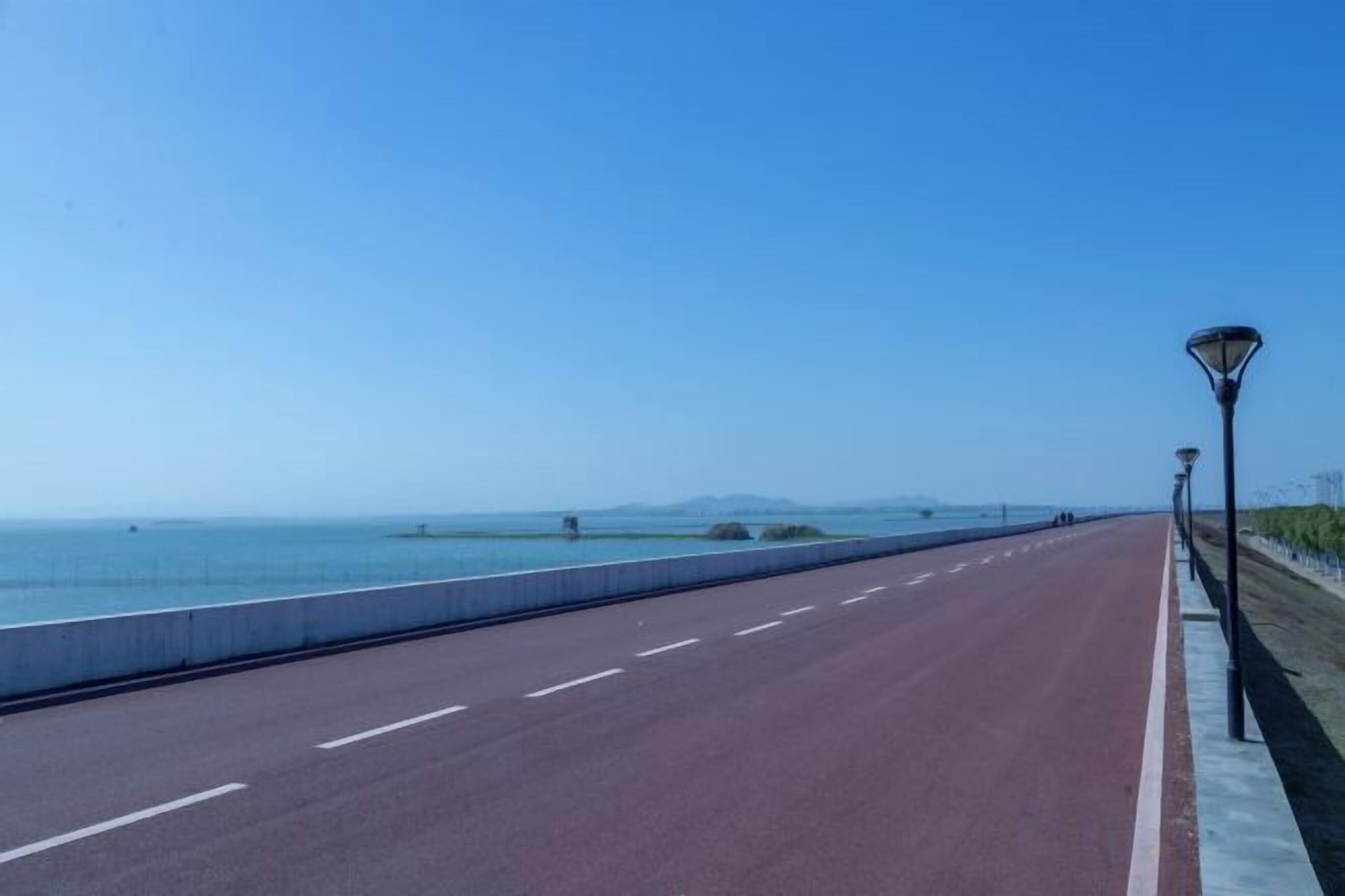 A coastal road with a clear sky, a paved path, and street lamps.