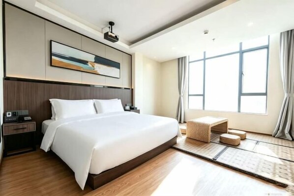Een hotelkamer met een groot bed, een nachtkastje, een wandtelevisie en een raam met gordijnen.