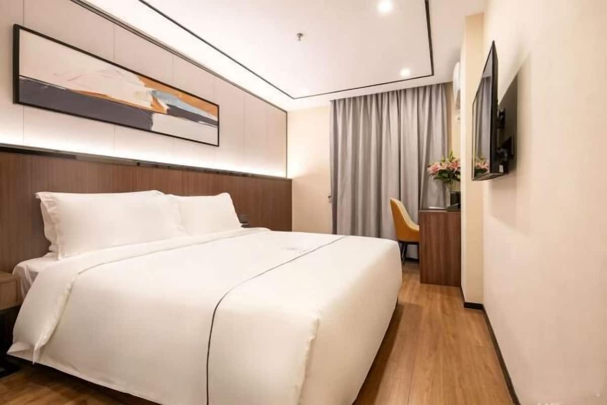 A modern hotel room with a large bed, a flat-screen TV, a desk with a chair, and a painting on the wall.