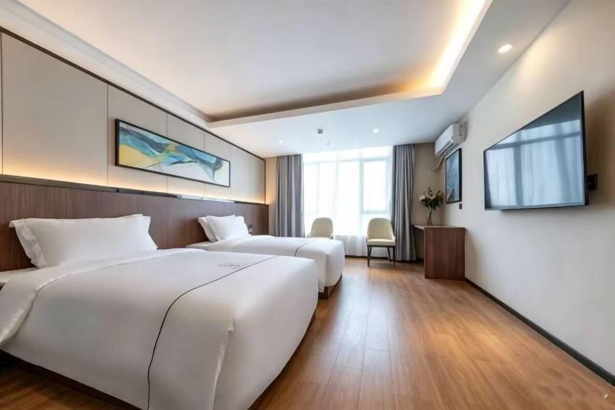 A hotel room with two beds, a desk, a chair, a TV, and artwork on the walls.