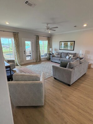 Ein geräumiges Wohnzimmer mit grauem Sofa, gemusterten Sesseln, einem Couchtisch und einem Deckenventilator.