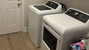 A laundry room with two front-loading washing machines and a dryer, white cabinets above, and a wooden floor.
