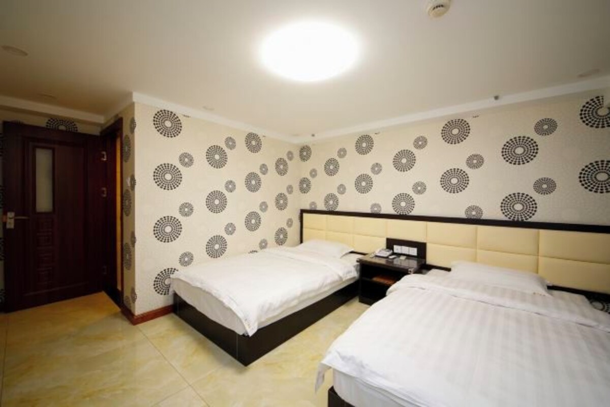 A hotel room with two beds, a wooden door, and patterned wallpaper.