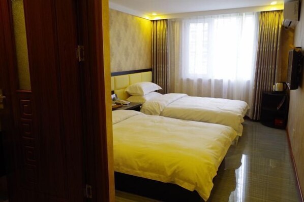 Habitación de hotel con dos camas, una mesita de noche, una lámpara, una ventana con cortinas y un televisor montado en la pared.