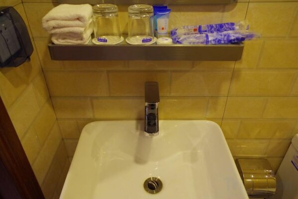 Un lavabo de salle de bain avec un robinet, une étagère au-dessus contenant des serviettes, un distributeur de savon et un bocal en verre.