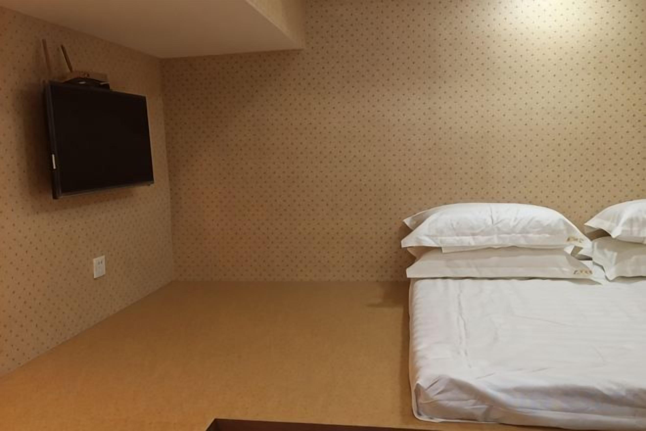 A room with a bed, a flat-screen TV mounted on the wall, and a patterned wall.